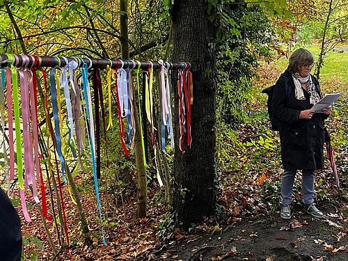 Die Bänder hängen an einer Stange zwischen zwei Bäume, vor dem Wasserschloß Werdringen. Eine Ehrenamtliche Kollegin aus dem Hospiz liest etwas dazu vor.